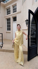 Model standing by a black door wearing a cream yellow sleeveless Cheongsam blouse and matching wide-leg palazzo pants.