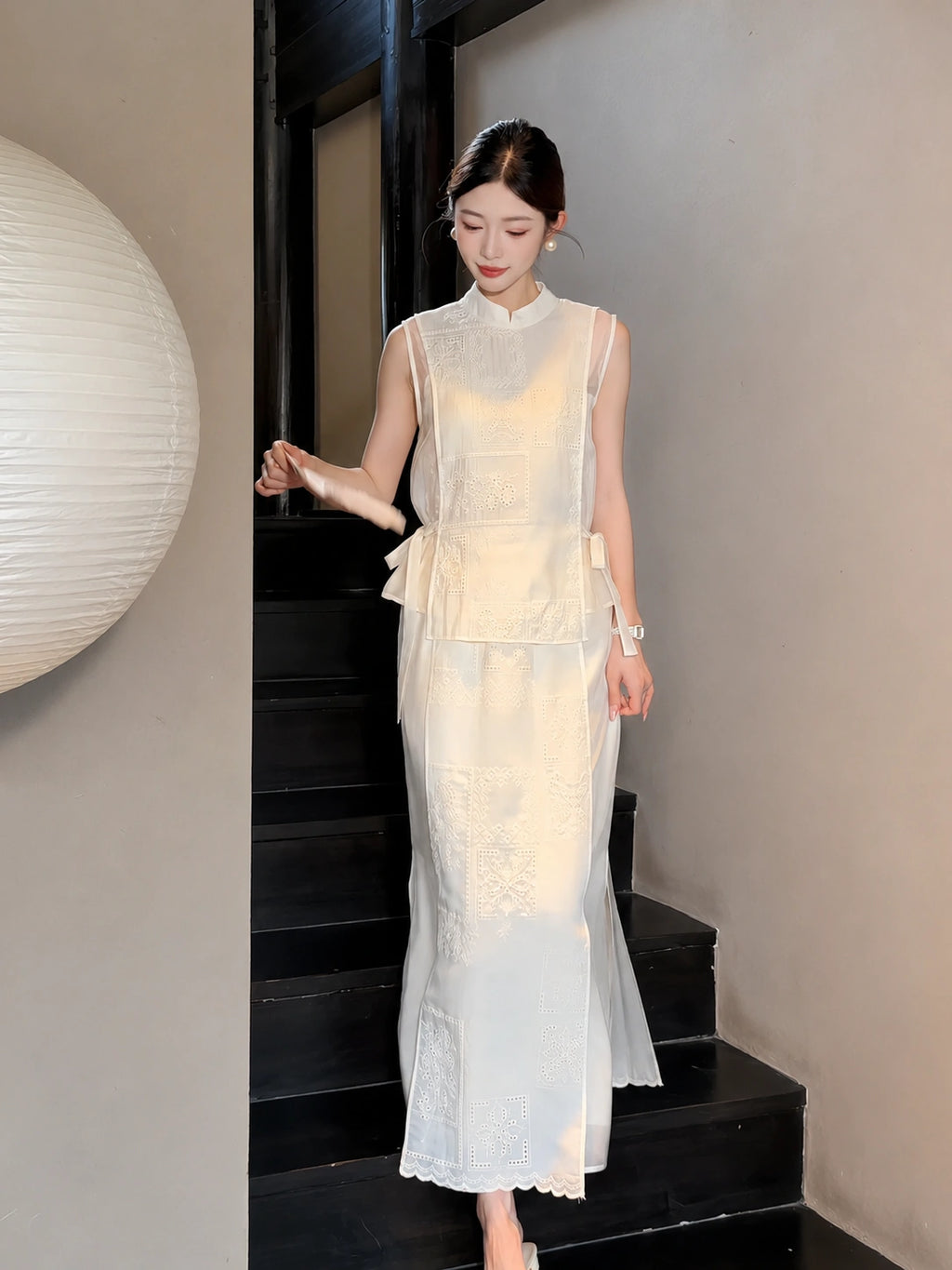 Model walking down stairs in a cream white A-line midi skirt and matching vest, showcasing the scalloped hem and side tie details.