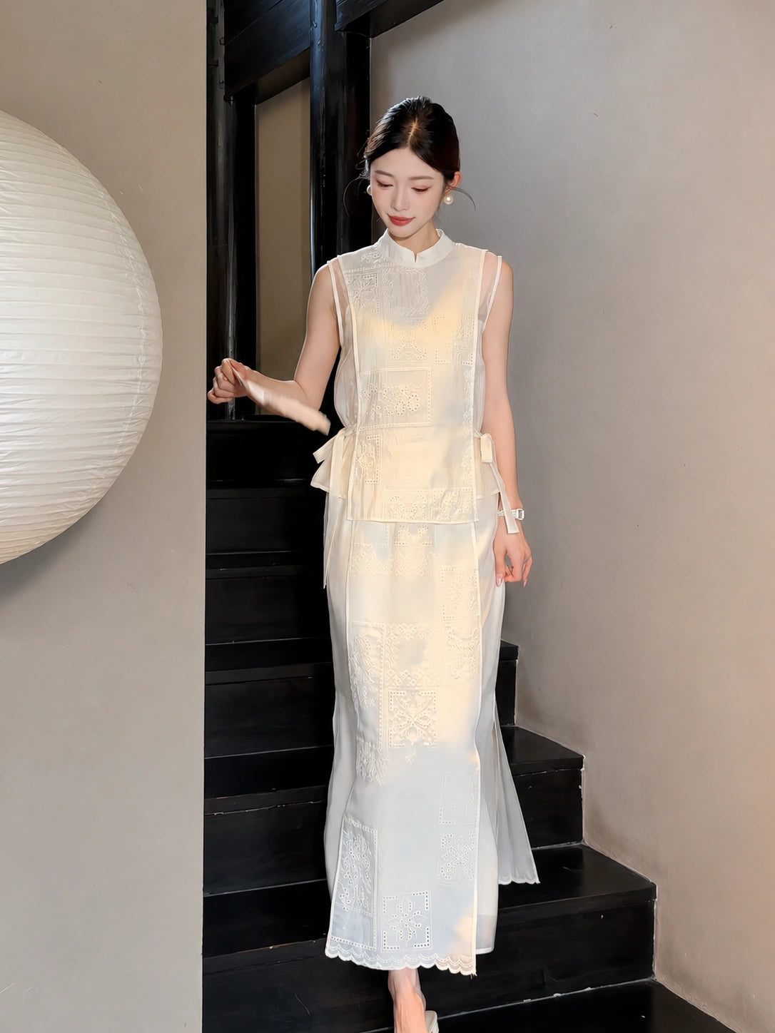 Model walking down stairs in a cream white A-line midi skirt and matching vest, showcasing the scalloped hem and side tie details.