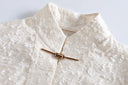 Close-up of the Ningzhi Ivory shirt’s stand collar, raised texture and gold-tone bar closure.