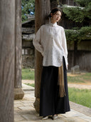 Model wearing the Ningzhi Ivory textured shirt with a black skirt beside a wooden pillar.