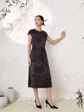 Full body shot of a dark abstract print silk midi dress with a round neckline, short cap sleeves, and a tie waist detail, crafted from 100% mulberry silk, styled with black heels.
