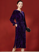 Angled view of the purple velvet midi dress on a model, showing the tied waist, long sleeves and side slit.