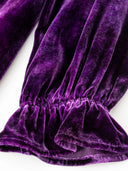 Close-up of a purple velvet sleeve gathered above its ruffled cuff.