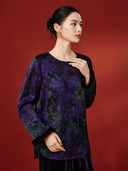 Angled view of the purple foliage-print blouse, showing the round neckline, relaxed shape and black cuff trim.