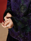 Close-up of black textured cuff trim on the purple blouse, beside green and teal leaf motifs.