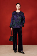 Full-length outfit with a purple foliage-print silk blouse, dark wide-leg trousers and a black handbag.