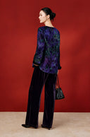 Back view of the purple foliage-print blouse on a model, showing its curved hem and long sleeves.