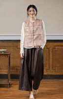 Full-length look of the dusty rose jacquard vest layered over a cream blouse with brown trousers.