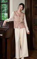 Model beside a piano wearing the rose vest with a cream blouse and wide-leg trousers.