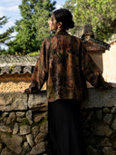 Back view of an earth brown printed jacket, showing its relaxed shape, long sleeves and olive green and black abstract motifs.