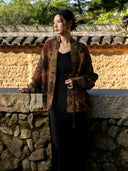 Model wearing an earth brown printed jacket open over a black dress, showing the front band and buttoned cuff details.