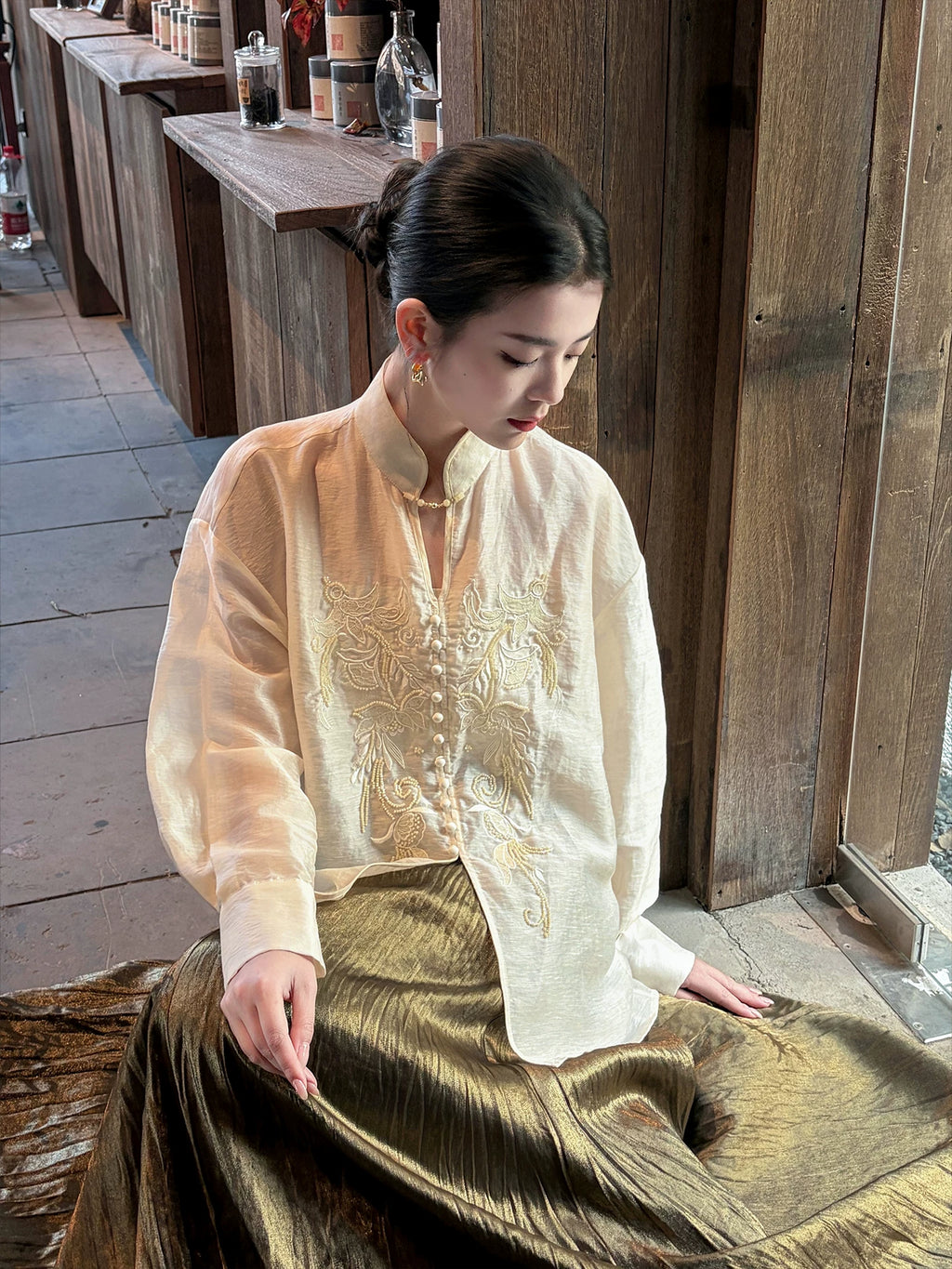 Woman wearing an embroidered mandarin collar linen blend blouse in a warm indoor lifestyle setting.