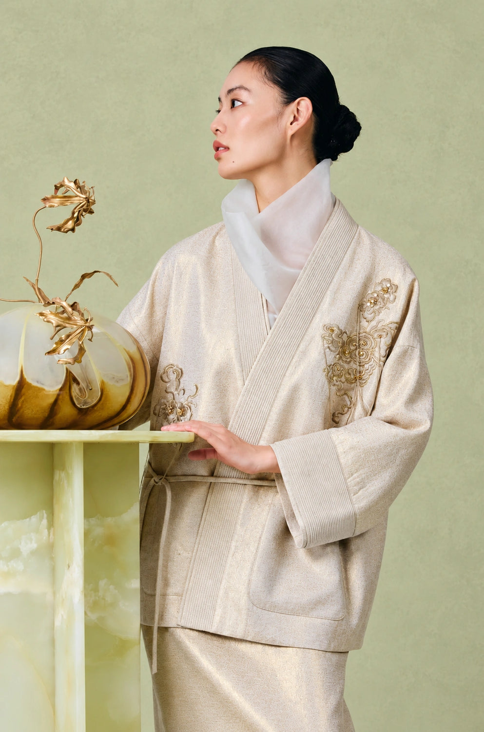 Detail of the champagne beige jacket’s V-neck, gold floral embroidery and wide sleeve cuff