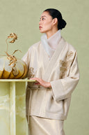 Detail of the champagne beige jacket’s V-neck, gold floral embroidery and wide sleeve cuff