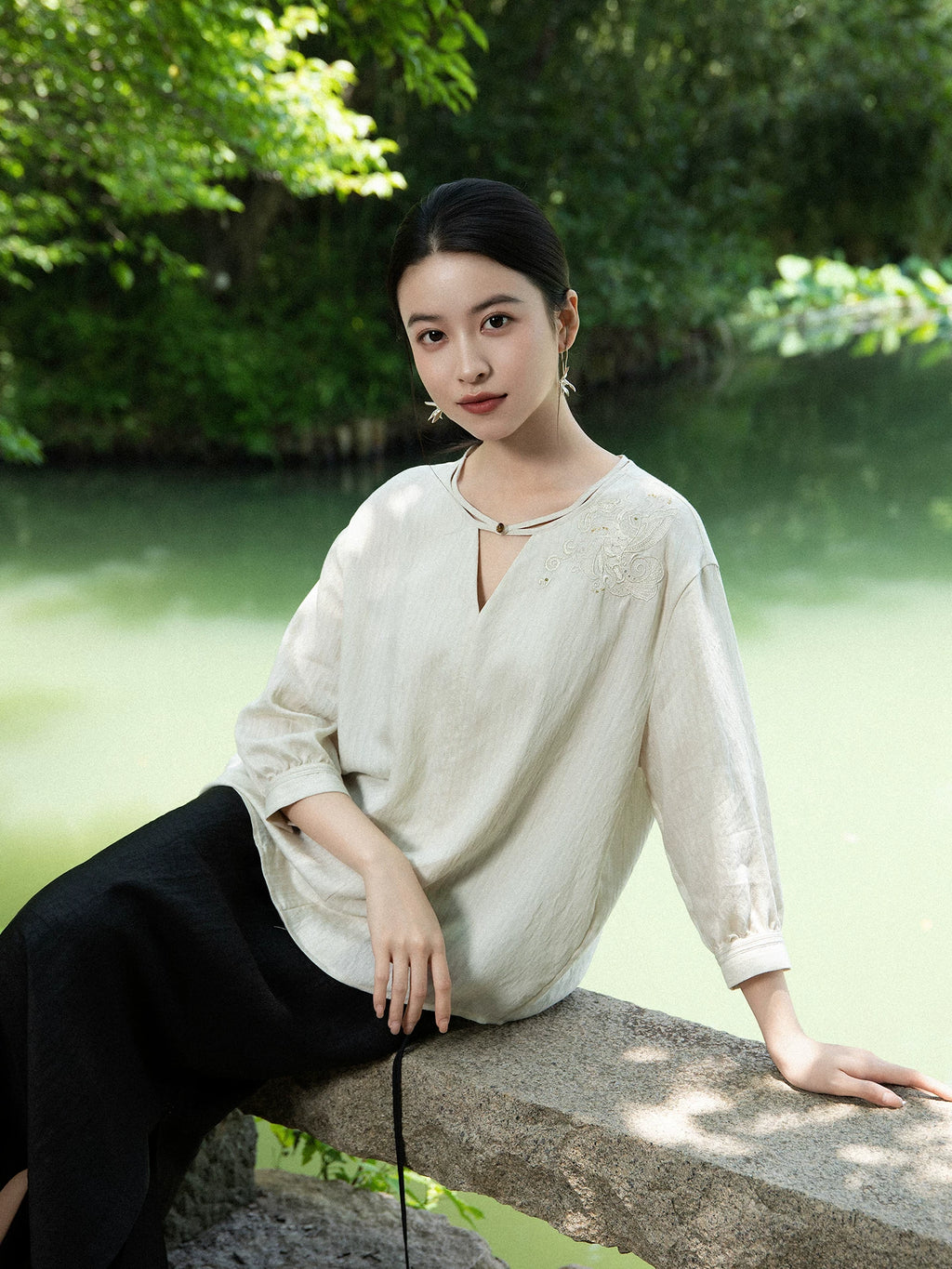 Women's embroidered blouse styled outdoors beside a peaceful lake.