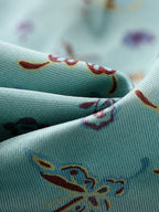 Close-up of aqua Shu brocade silk woven with colorful butterfly and botanical motifs.