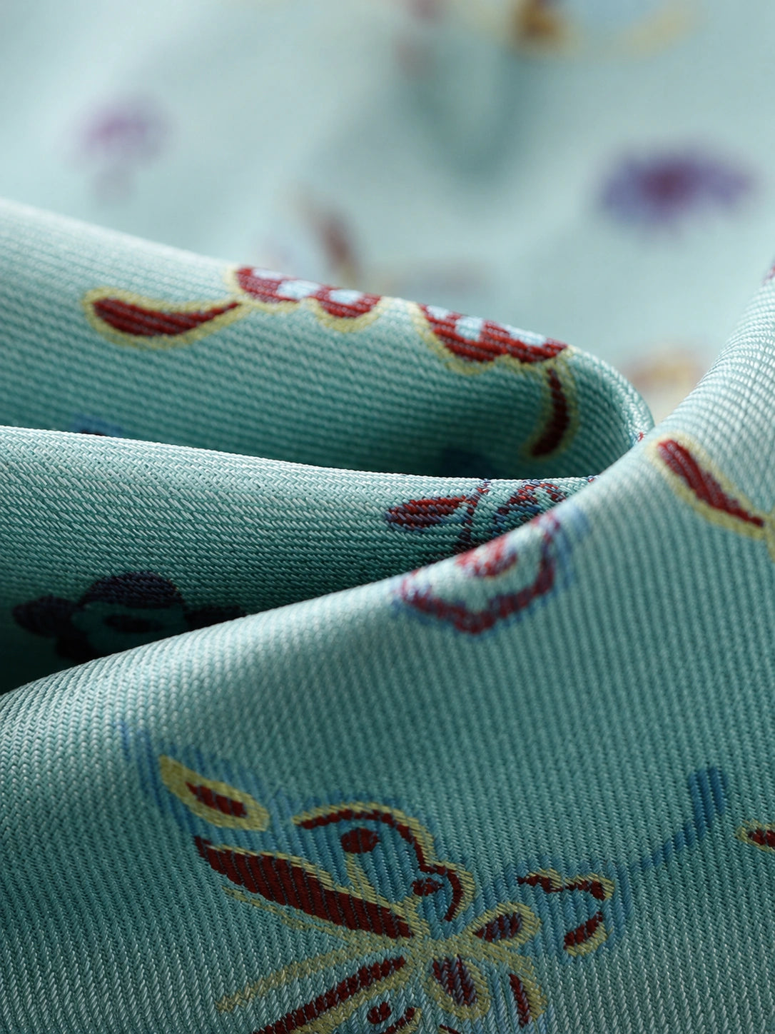 Close-up of aqua Shu brocade silk woven with colorful butterfly and botanical motifs.