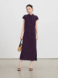 Woman wearing an ankle-length aubergine silk qipao dress styled with a woven handbag.
