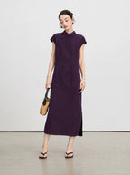 Woman wearing an ankle-length aubergine silk qipao dress styled with a woven handbag.