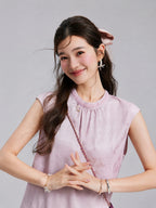 Close view of the beaded round neckline and gathered front of a blush-lilac jacquard top.