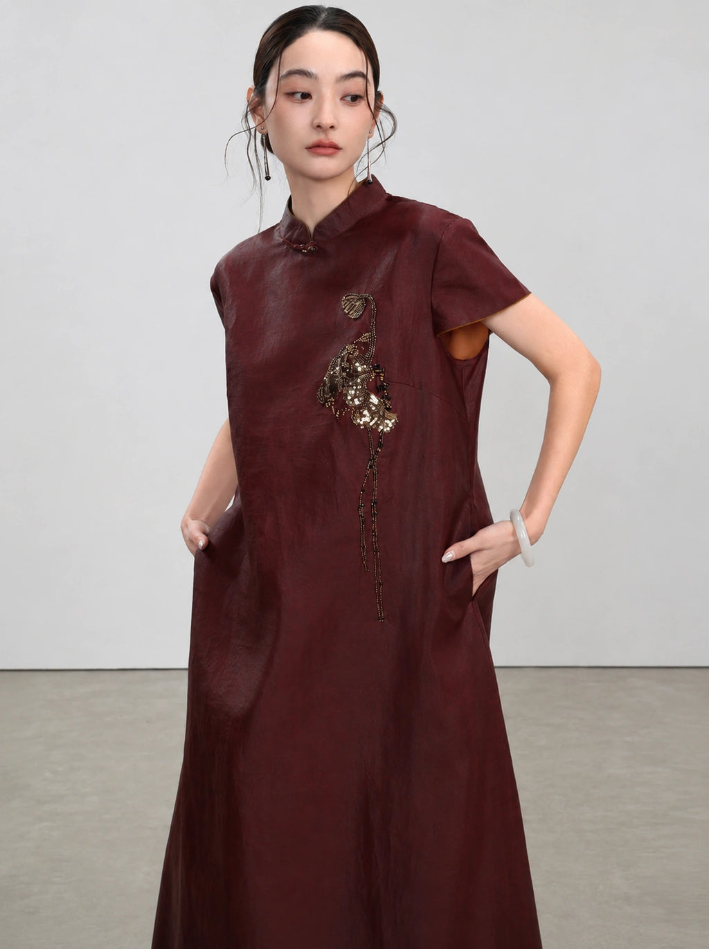 Three-quarter view showing the bronze beaded embroidery and side pockets of the Xiangyunsha dress