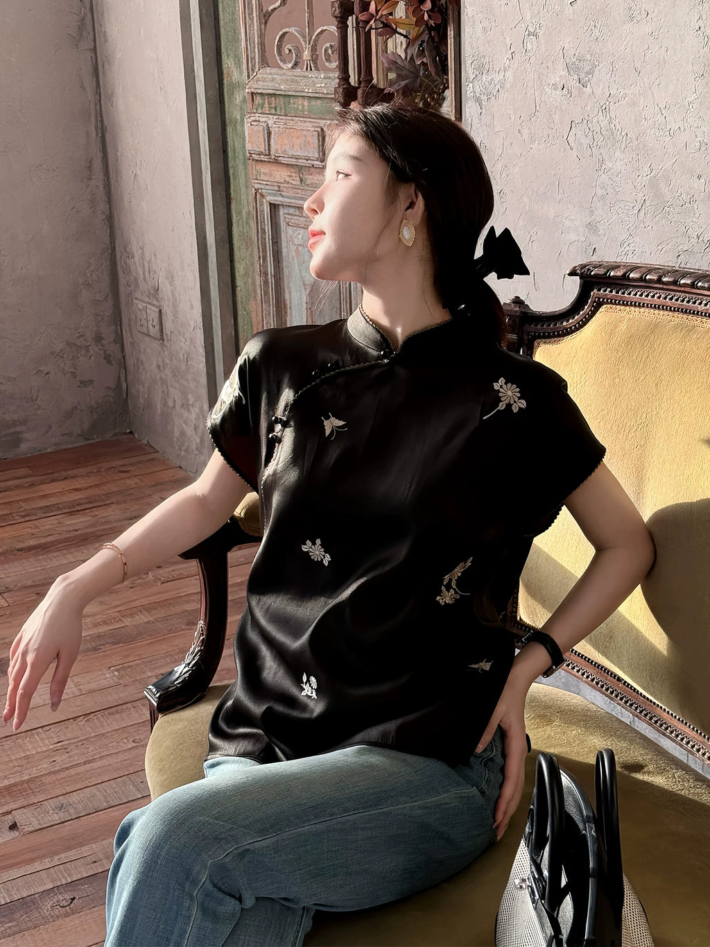 Model wearing a black mulberry silk top with floral embroidery and flutter sleeves