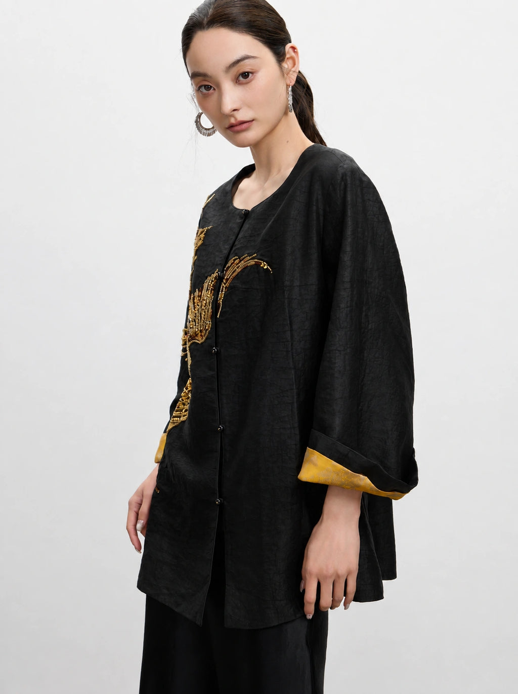 Close-up of the relaxed black silk jacket with gold embroidery and contrasting inner cuff detail.