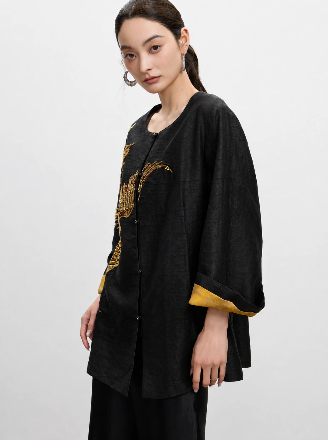 Close-up of the relaxed black silk jacket with gold embroidery and contrasting inner cuff detail.