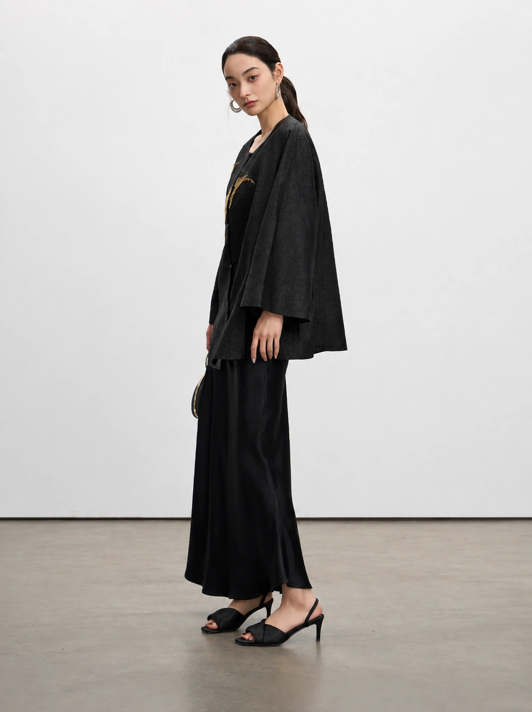 Side view of the relaxed black Gambiered Silk jacket showing its wide sleeves and textured silk fabric.