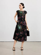 Black floral silk midi dress styled with a bamboo-handle handbag and flat sandals.