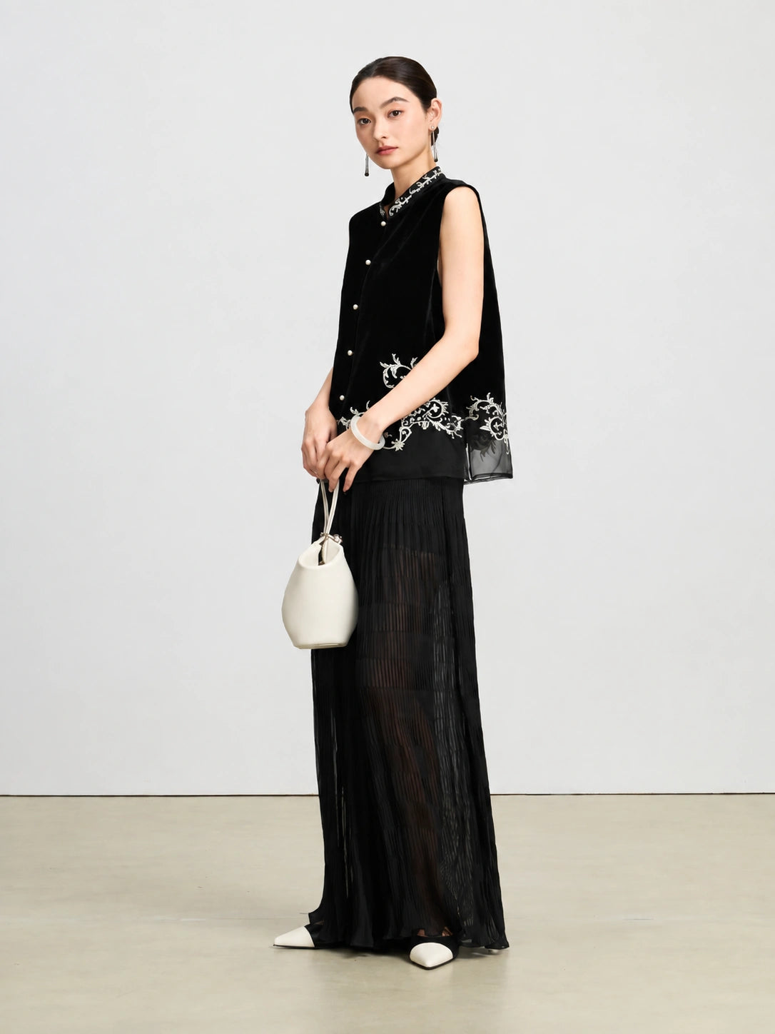 Three-quarter view of a jet-black velvet vest featuring ivory botanical embroidery and pearl-style buttons.