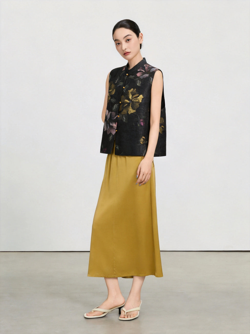 Model wearing a black hand-painted floral silk vest with a mustard yellow maxi skirt.