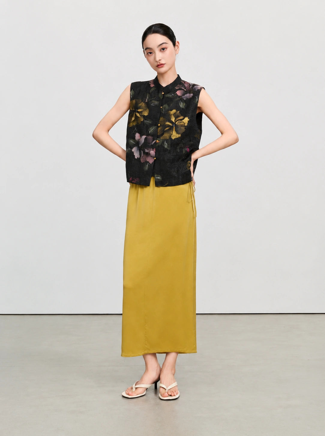Full-length styling of a sleeveless black floral silk vest paired with a mustard yellow skirt.