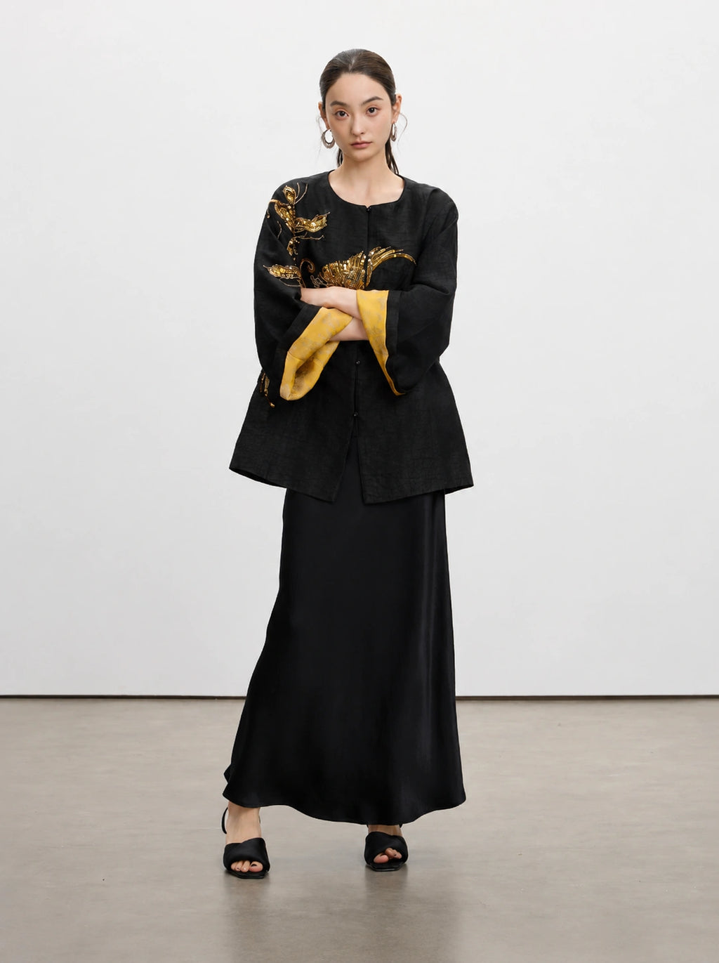 Close-up of the round neckline, covered button and tortoiseshell-inspired texture of the black silk jacket.