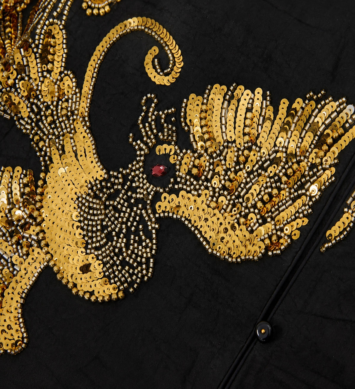 Detailed view of gold sequins and bead embroidery arranged in an ornate floral motif on black silk.