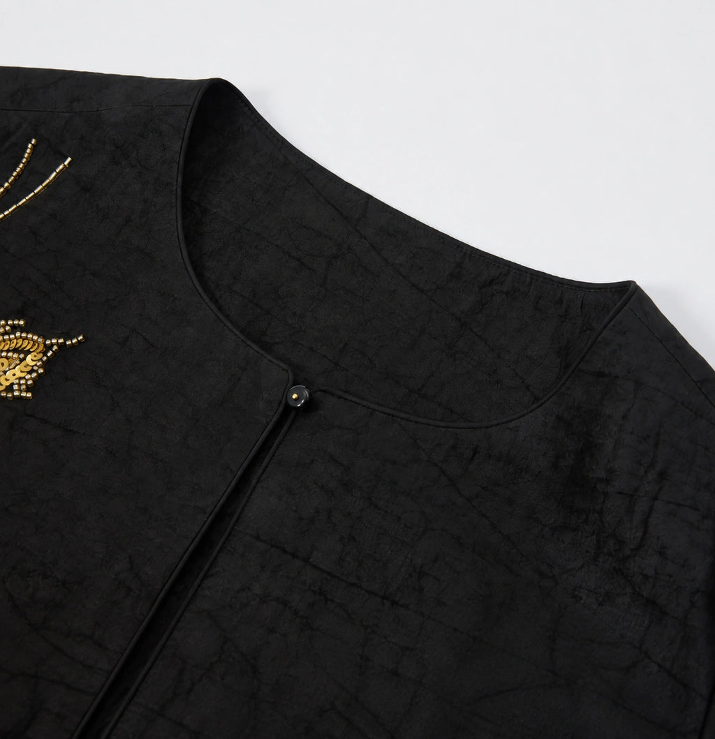 Close-up of the round neckline, covered button and tortoiseshell-inspired texture of the black silk jacket.