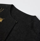 Close-up of the round neckline, covered button and tortoiseshell-inspired texture of the black silk jacket.