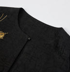Close-up of the round neckline, covered button and tortoiseshell-inspired texture of the black silk jacket.