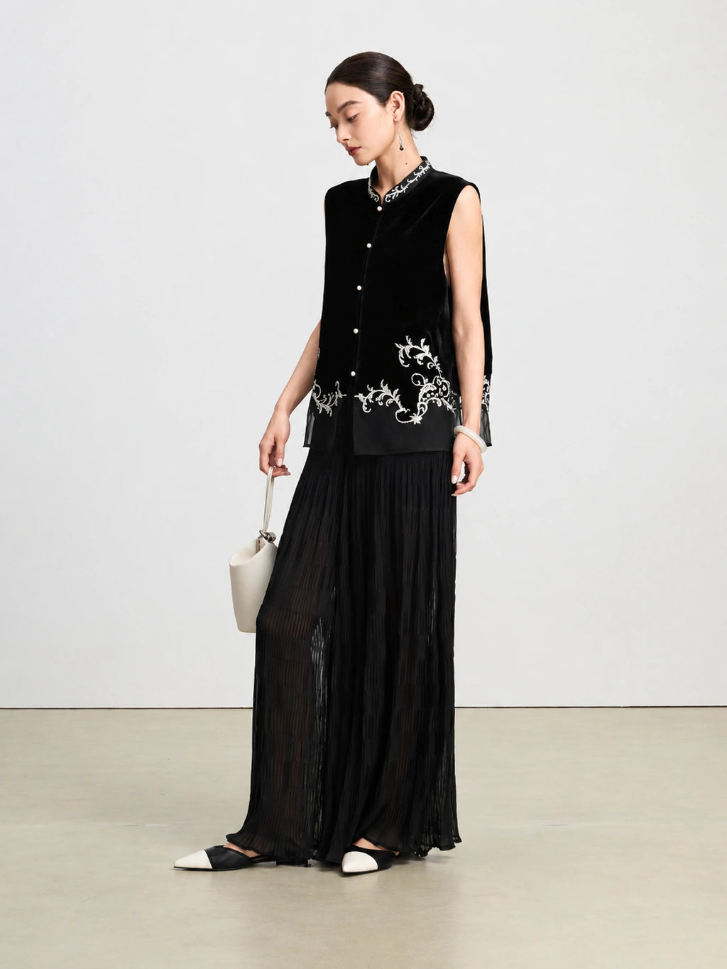 Model styling a black sleeveless silk vest with an embroidered Mandarin collar and floral hem.