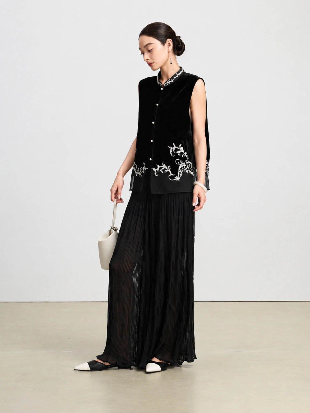 Model styling a black sleeveless silk vest with an embroidered Mandarin collar and floral hem.
