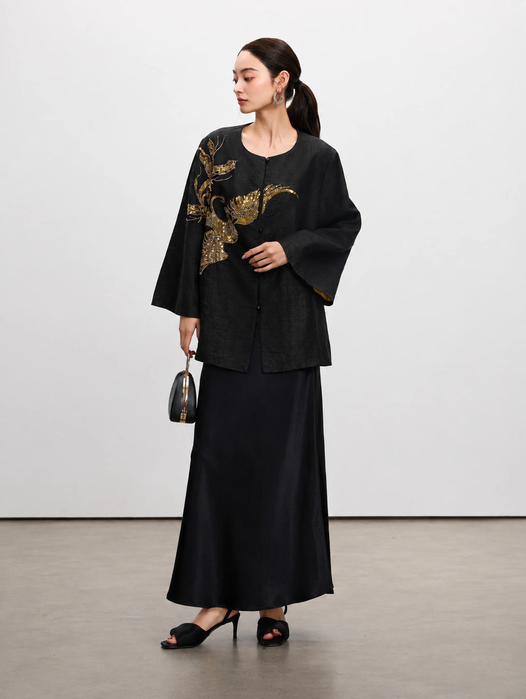 Model wearing a black mulberry silk jacket with gold sequin floral embroidery and a long black skirt.