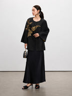 Model wearing a black mulberry silk jacket with gold sequin floral embroidery and a long black skirt.