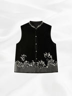 Front view of a black silk velvet vest with a Mandarin collar, pearl-style buttons and ivory embroidery.