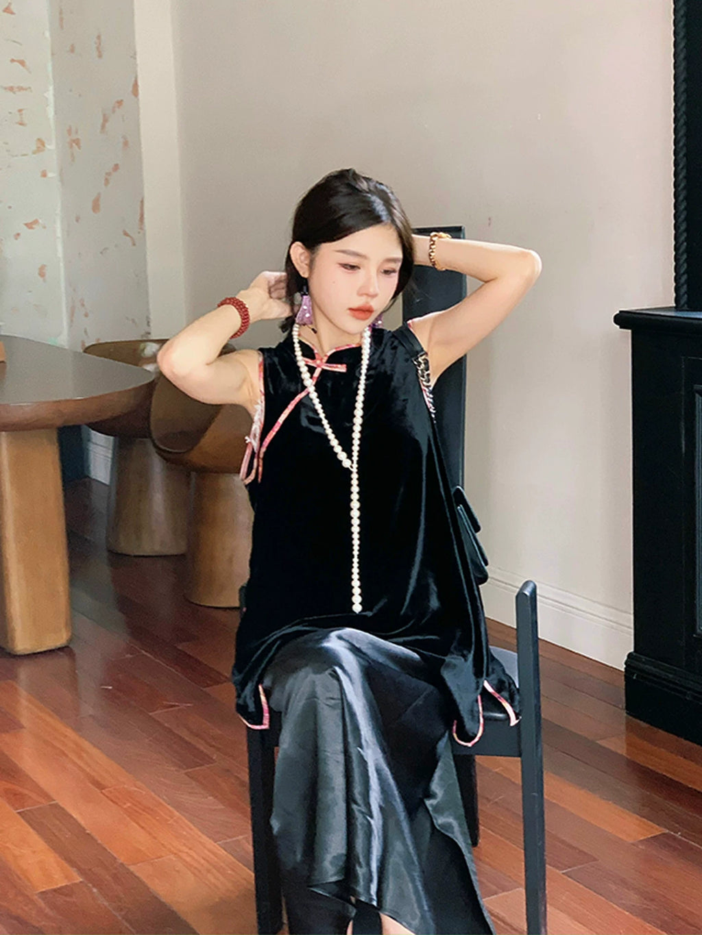 Model wearing a black Chinese-inspired sleeveless tunic top with pink contrast piping