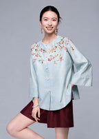 Closer front view of the powder blue cardigan showing the berry and bird embroidery across the shoulders.