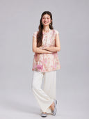 Model wearing a Gambiered Silk blush floral embroidered longline top with white wide-leg trousers