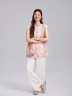 Model wearing a Gambiered Silk blush floral embroidered longline top with white wide-leg trousers