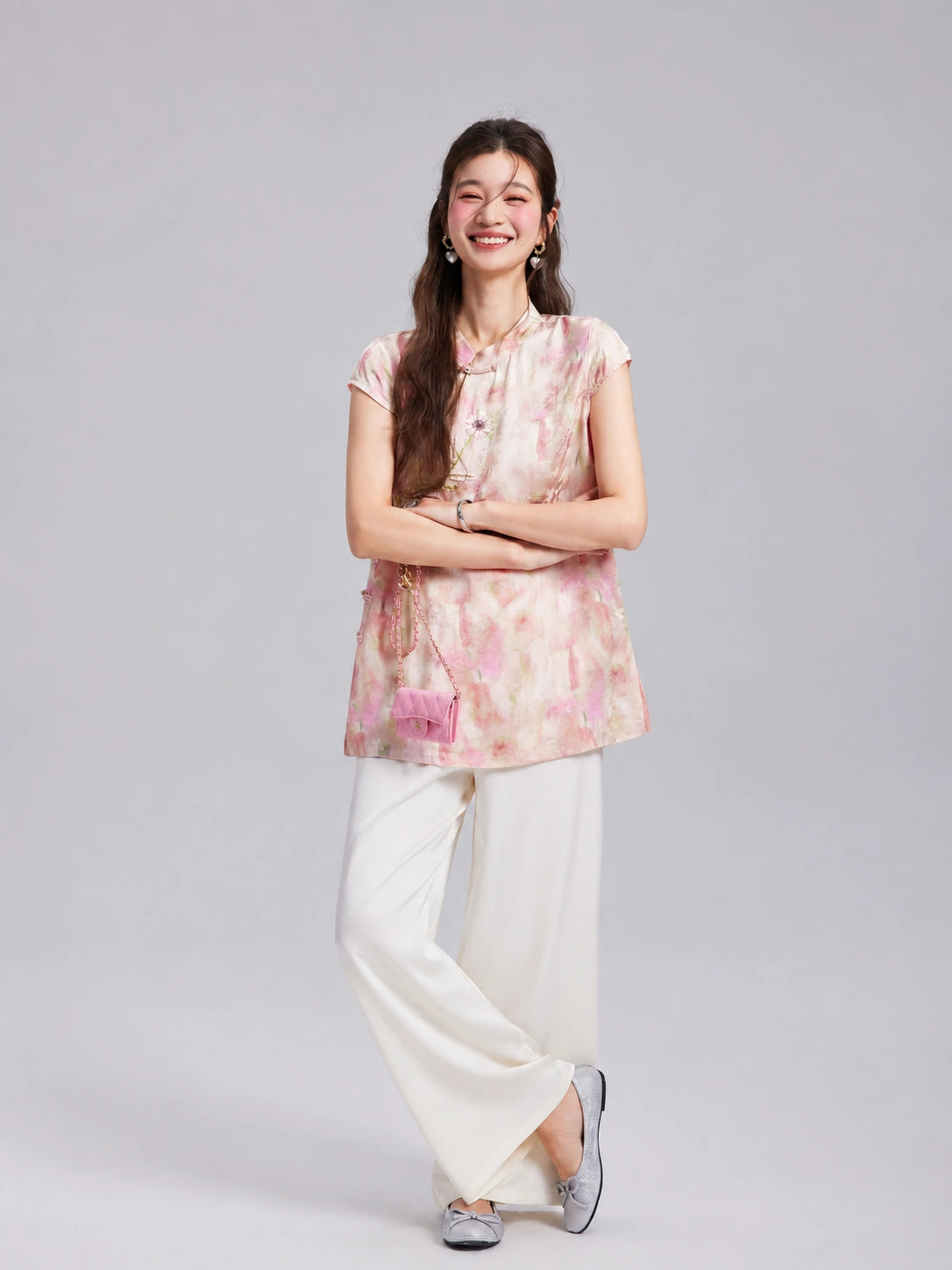 Model wearing a Gambiered Silk blush floral embroidered longline top with white wide-leg trousers