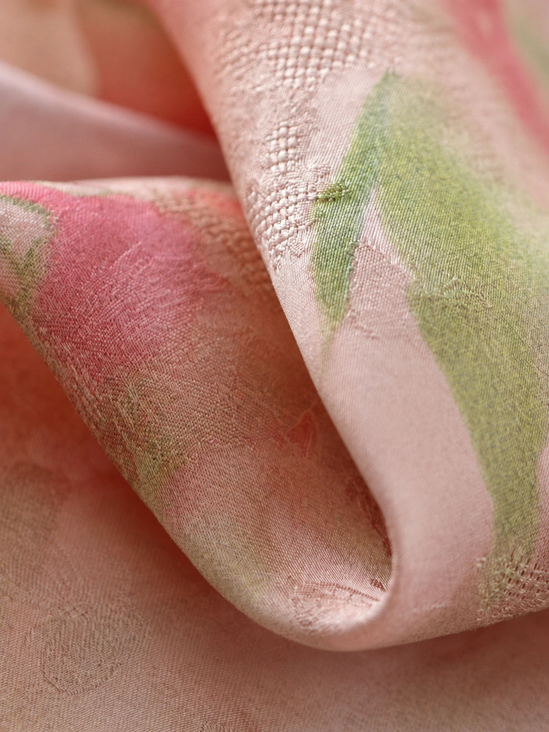 Close-up of blush pink textured fabric with watercolor-effect pink flowers, green leaves and subtle woven motifs